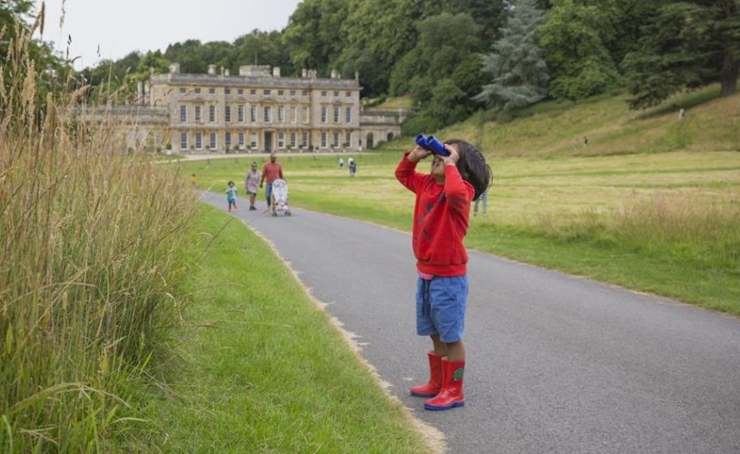 Child looking through binoculars with a view of Dyrham Park house in the background